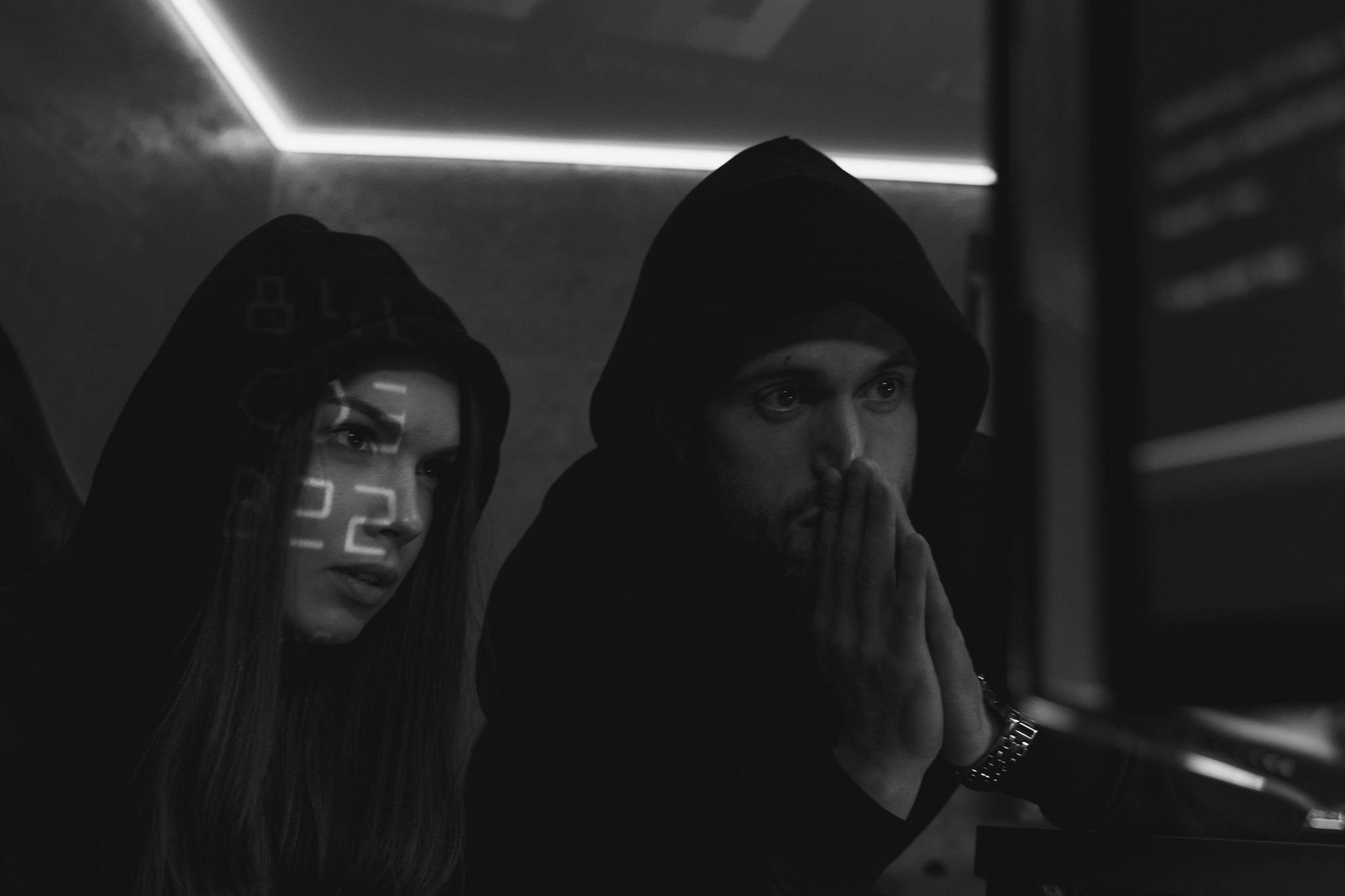 Two cybersecurity experts in hoodies study data on screens in a dimly lit room, symbolizing cyber defense.